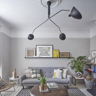 house plants on side tables in grey living room with large hanging lights and grey sofa with coloured cushions