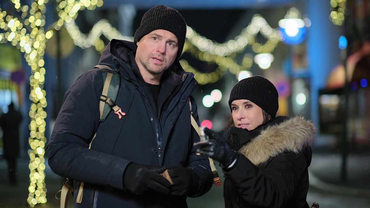 Kristoffer Polaha and Lacey Chabert outside in coats and hats in Iceland for The Christmas Quest filming.