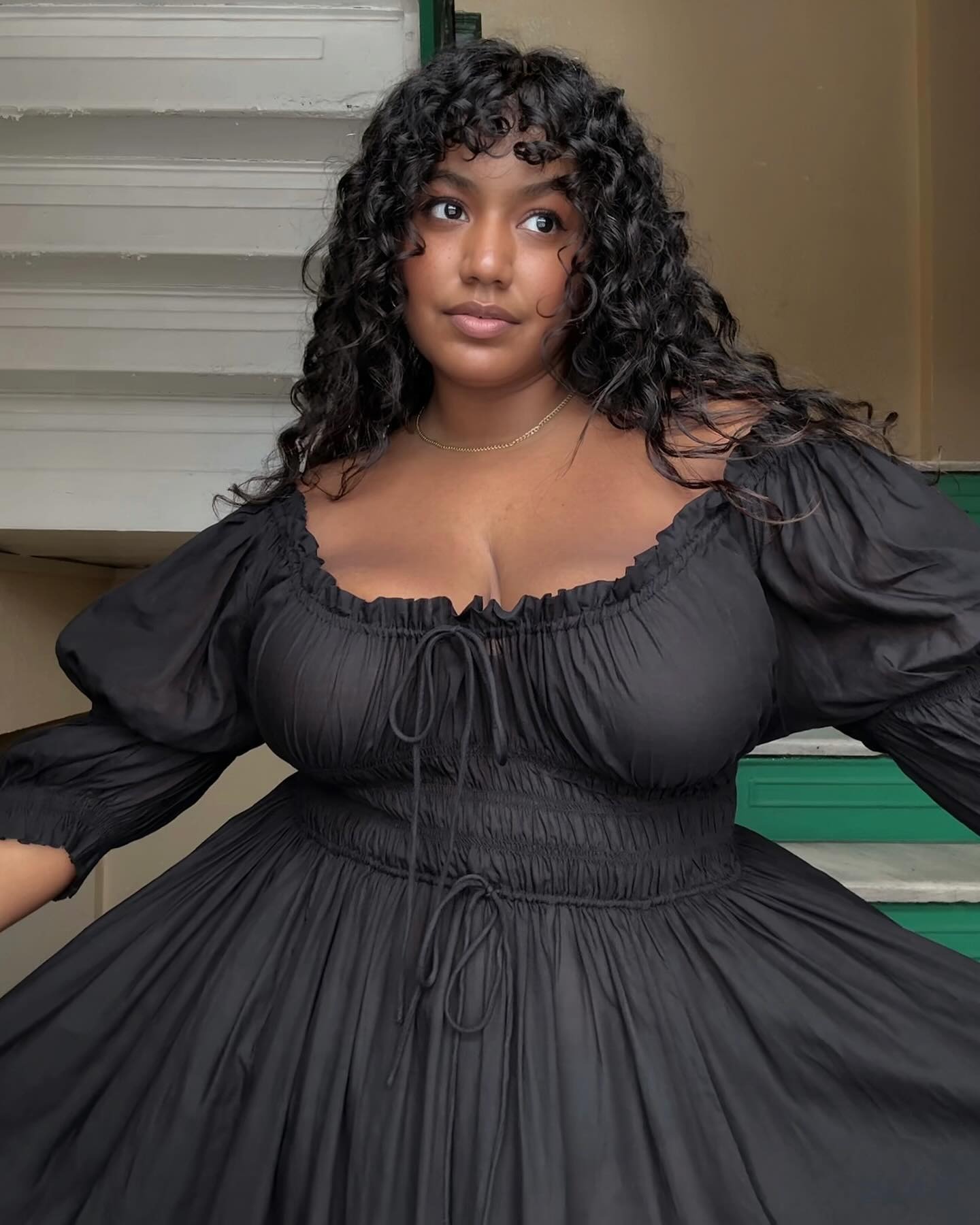 A woman wearing a black long-sleeved dress and curly hair with bangs.