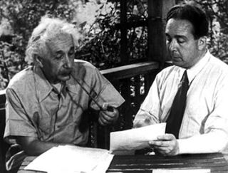 Einstein on the left and Szilard on the right look at pieces of paper.