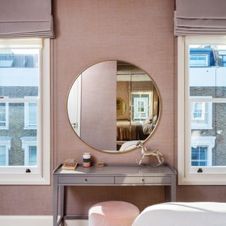 dressing table with round mirror between windows in pink bedroom