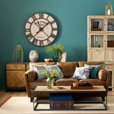 living room with forest green wall brown sofa with designed cushion clock on wall and wooden drawer