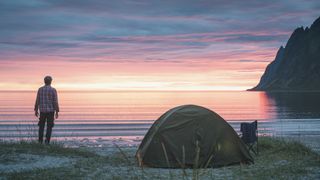 A man standing next to his tent at the beach looks out to sea