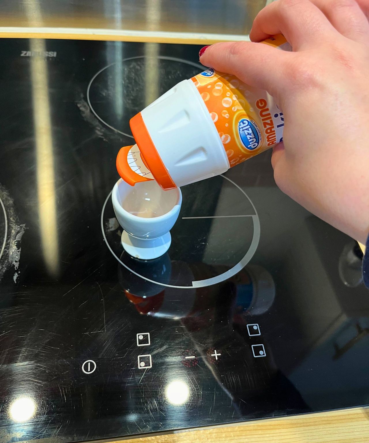 Me pouring baking soda from a plastic bottle with resealable lid into an egg cup on my black glass electric stop top