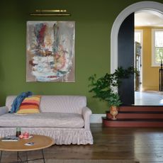 A green living room with an arched doorway painted in Sap Green by Farrow & Ball