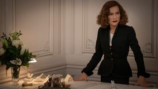 isabelle Huppert stands at her desk, dressed in black, in Mrs. Harris Goes to Paris.