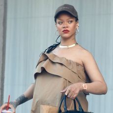 Rihanna wearing a brown strapless maxi dress, black baseball cap, and black leather bag in Los Angeles