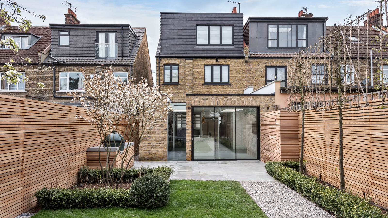 external view from garden of black slate clad loft conversion on semi detached brick house with additional single storey rear extension with black framed patio doors