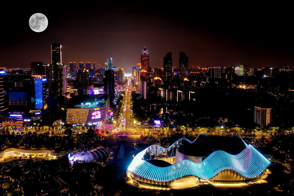 A silver sphere above a city illuminated with neon pink, yellow and blue hues