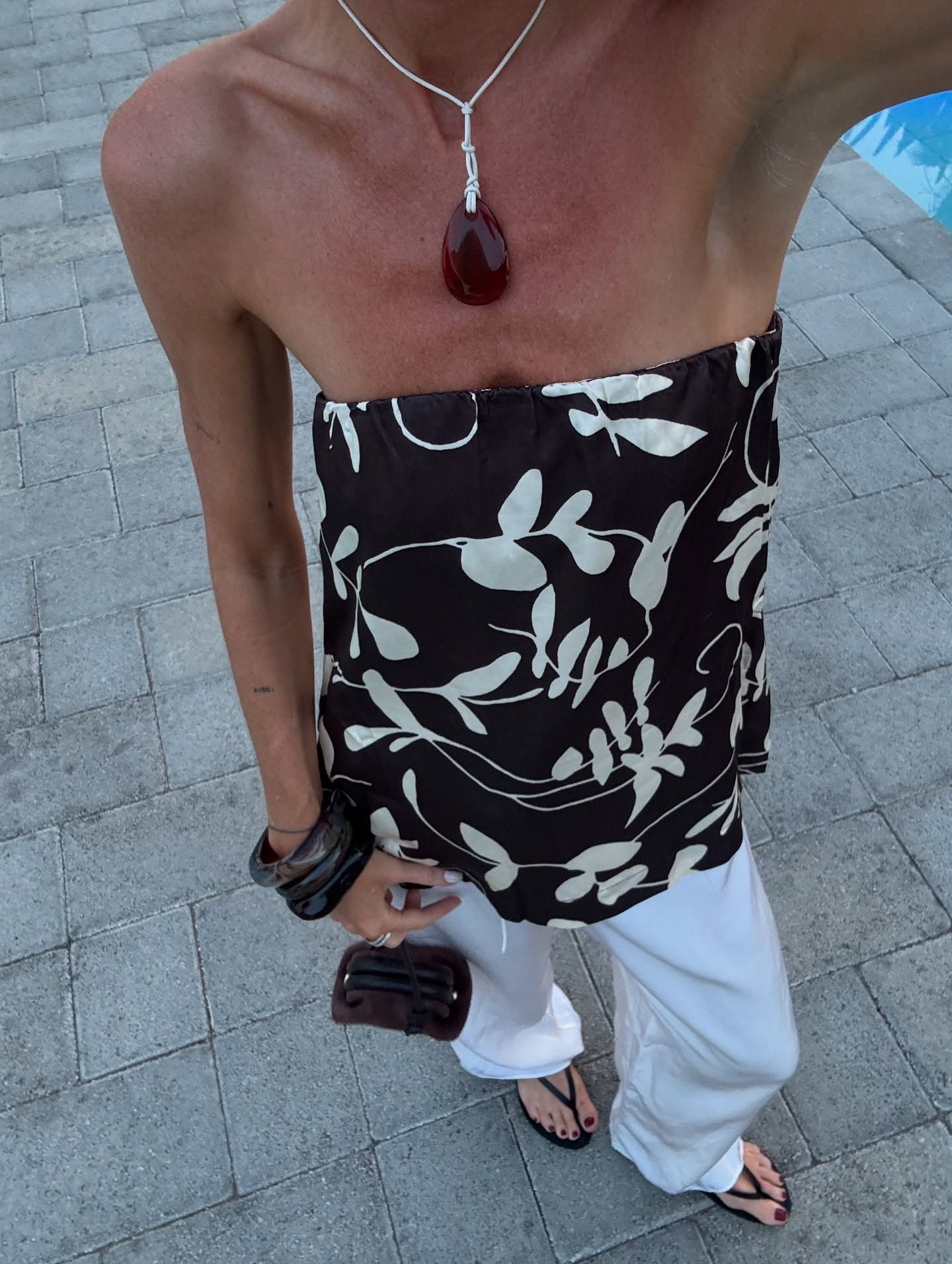 Hannah Lewis wears a pebble pendant, bandeau top, white trousers and flip flops