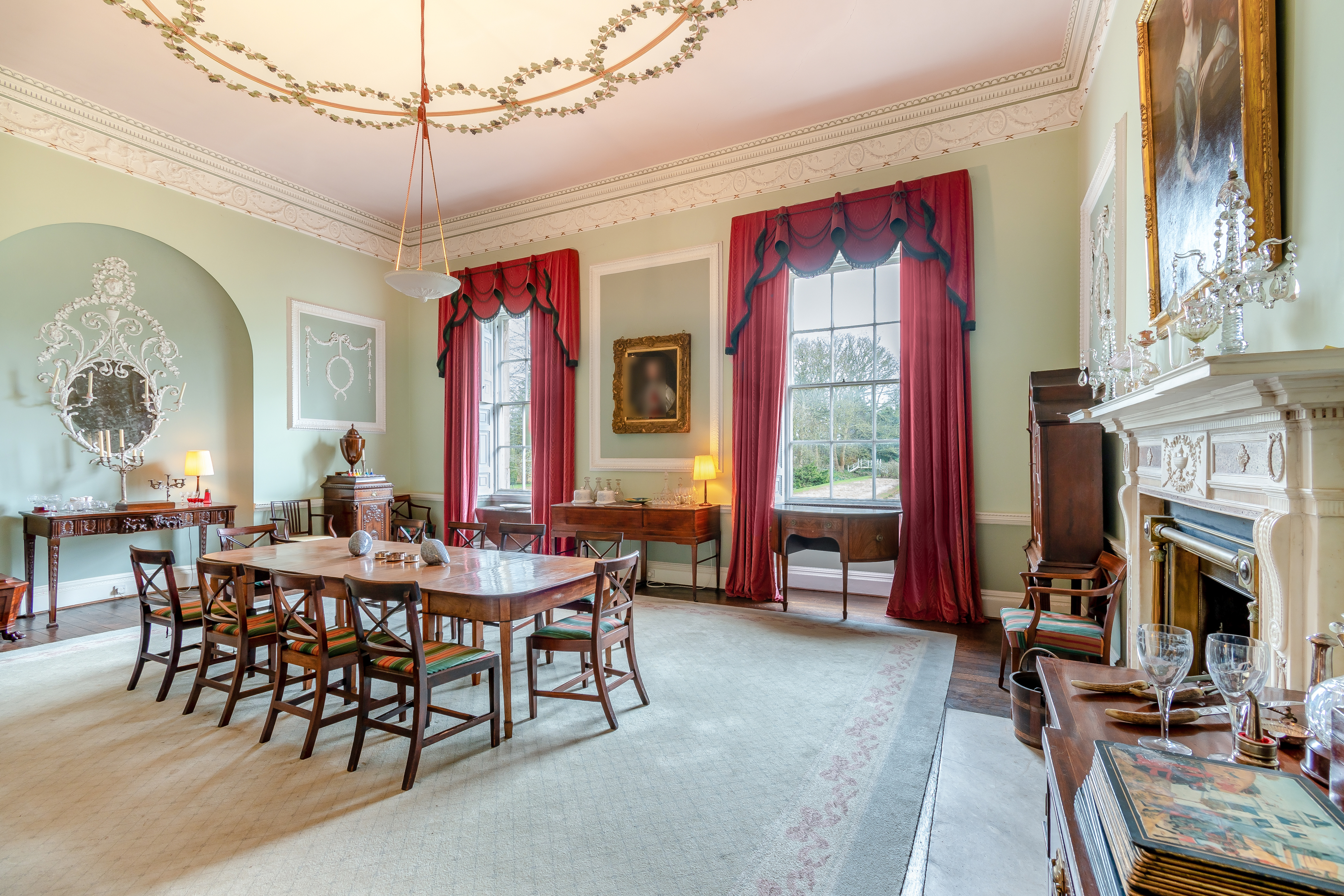 A dining room with a long dark wooden table and majestic red curtains