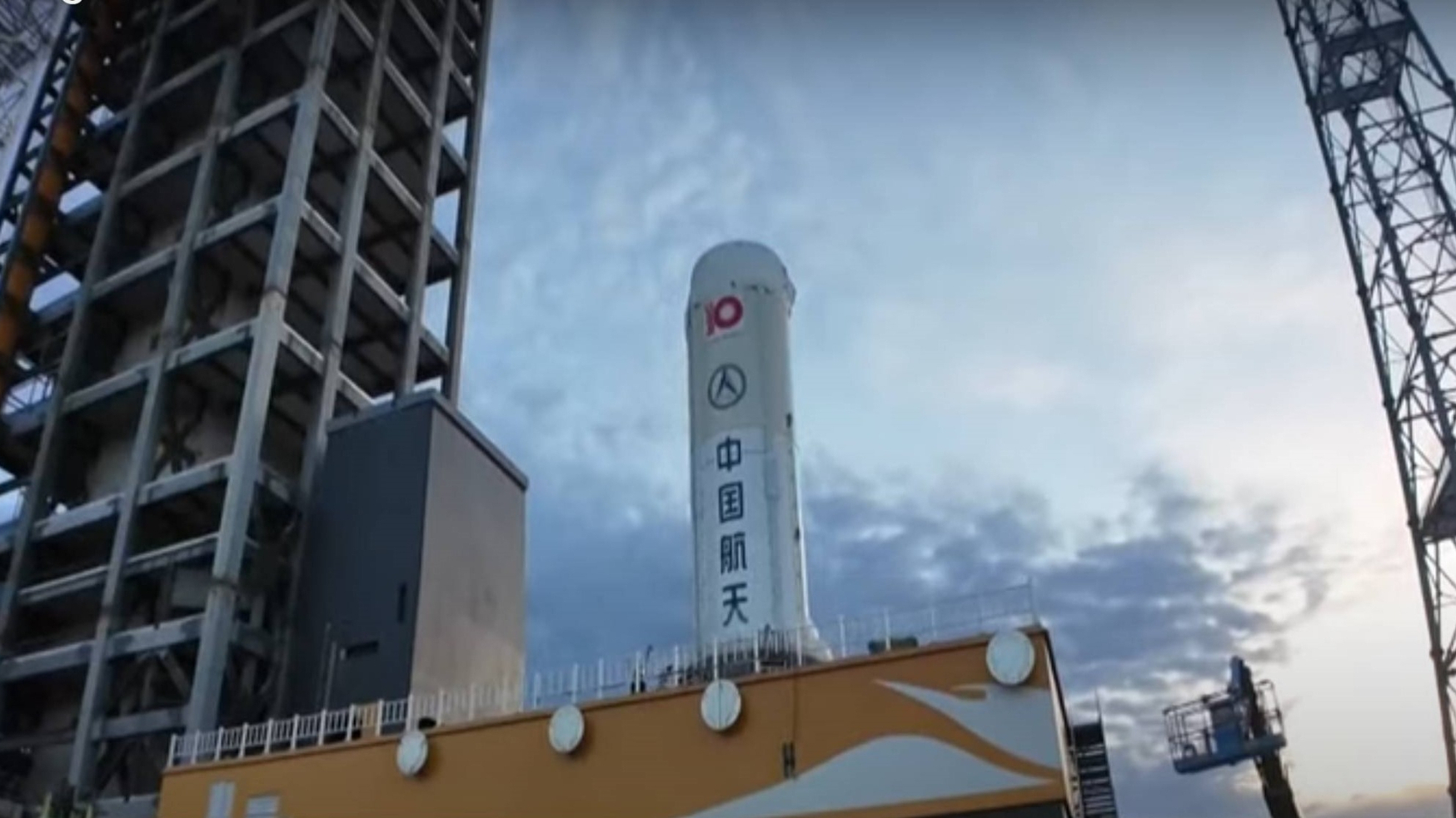 view looking up at a white rocket on a test stand beneath cloudy skies