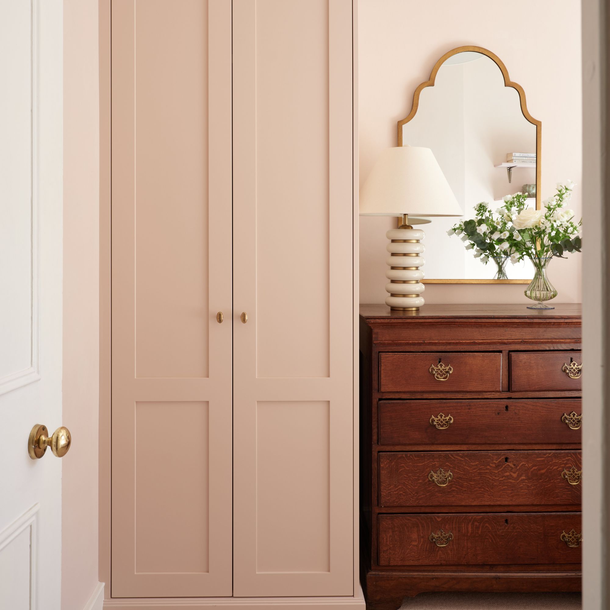 small two doored pink fitted wardrobe next to antique brown wooden chest of drawers