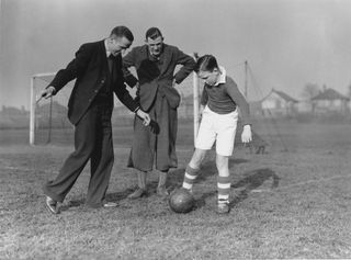 Liverpool player Matt Busby (left) gives some advice to youngster Len Langford (right) while his father, the Manchester City goalkeeper also named Len Langford, watches on.