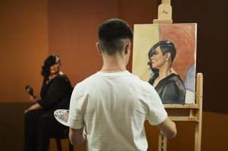 Singer Gabrielle poses while a contestant in the foreground paints her portrait in profile