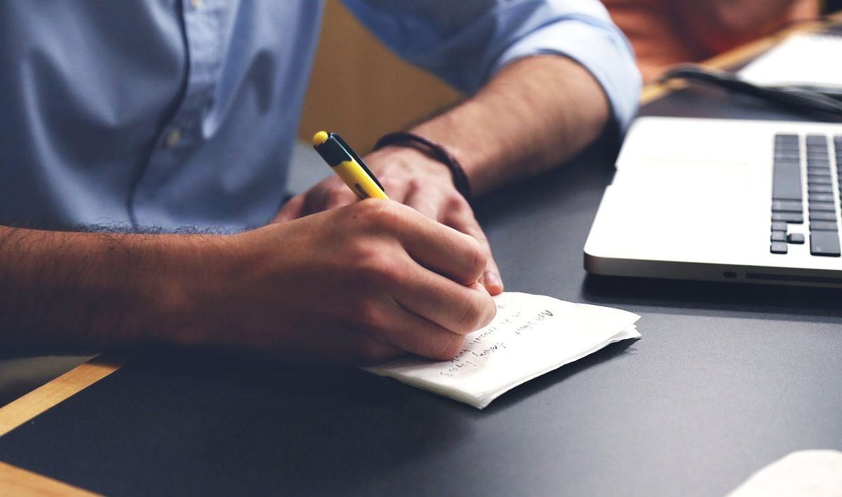 Man taking notes with pencil next to laptop computer