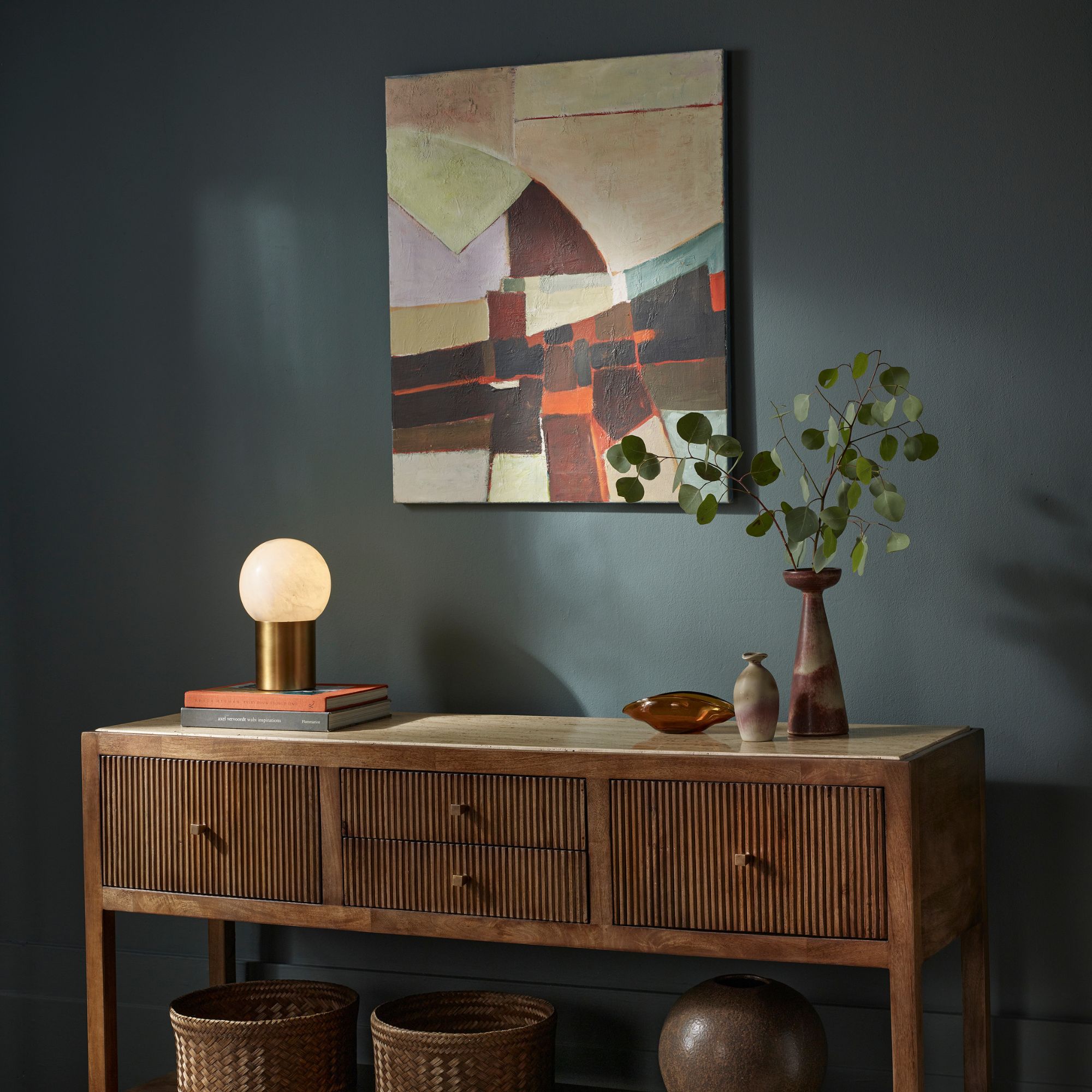 A dark blue wall with a mango wood side table against it and an abstract print on the wall