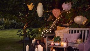 Colored lanterns hanging from tree, with twinkling fairy lights, and boho cushions on bench.