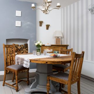 A dining room with grey and white striped wallpaper, a blue feature wall and a wooden dining table