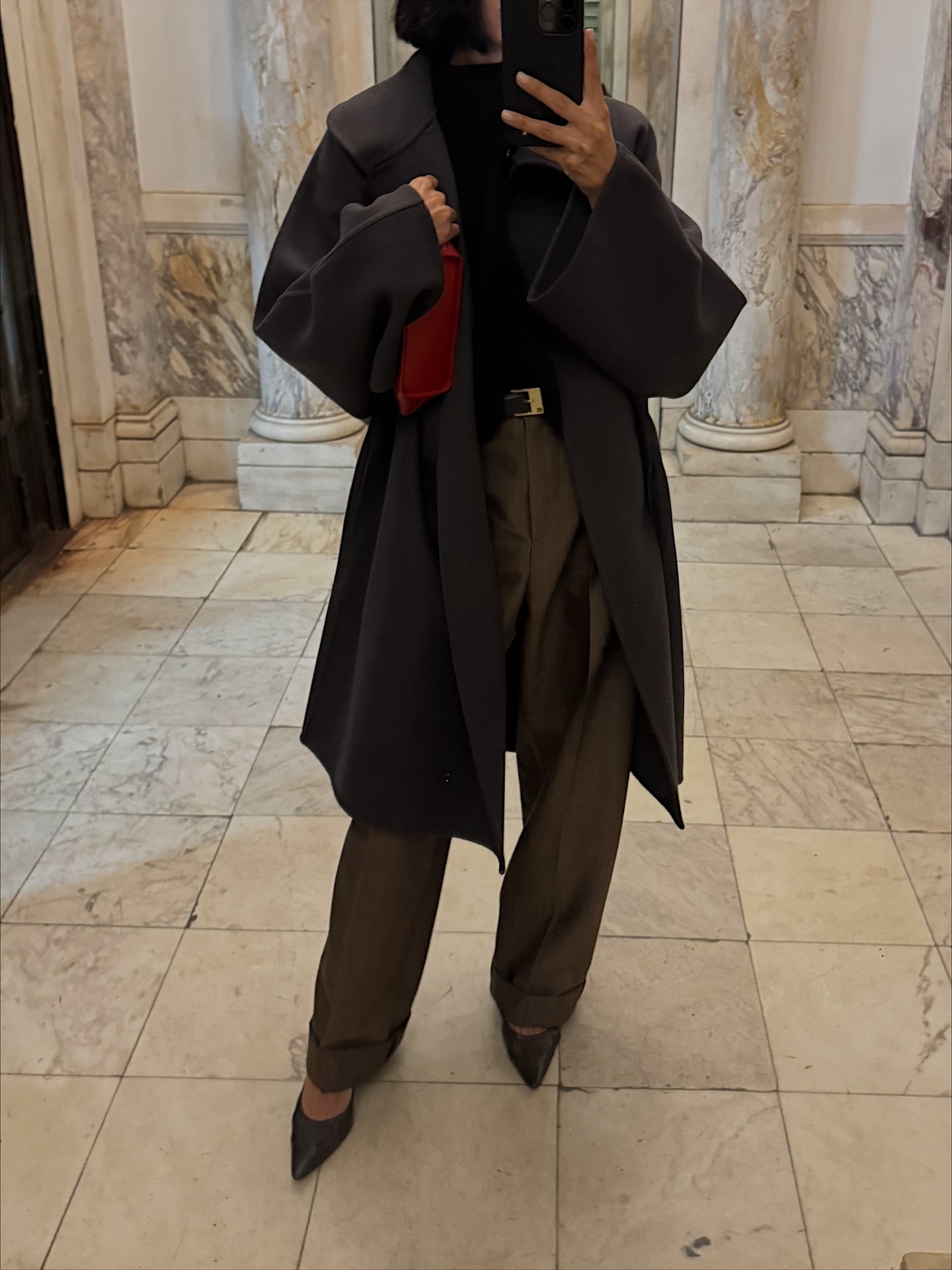 Shay wears a gray coat, black top, red clutch, dark green trousers, and black pointed-toe pumps.