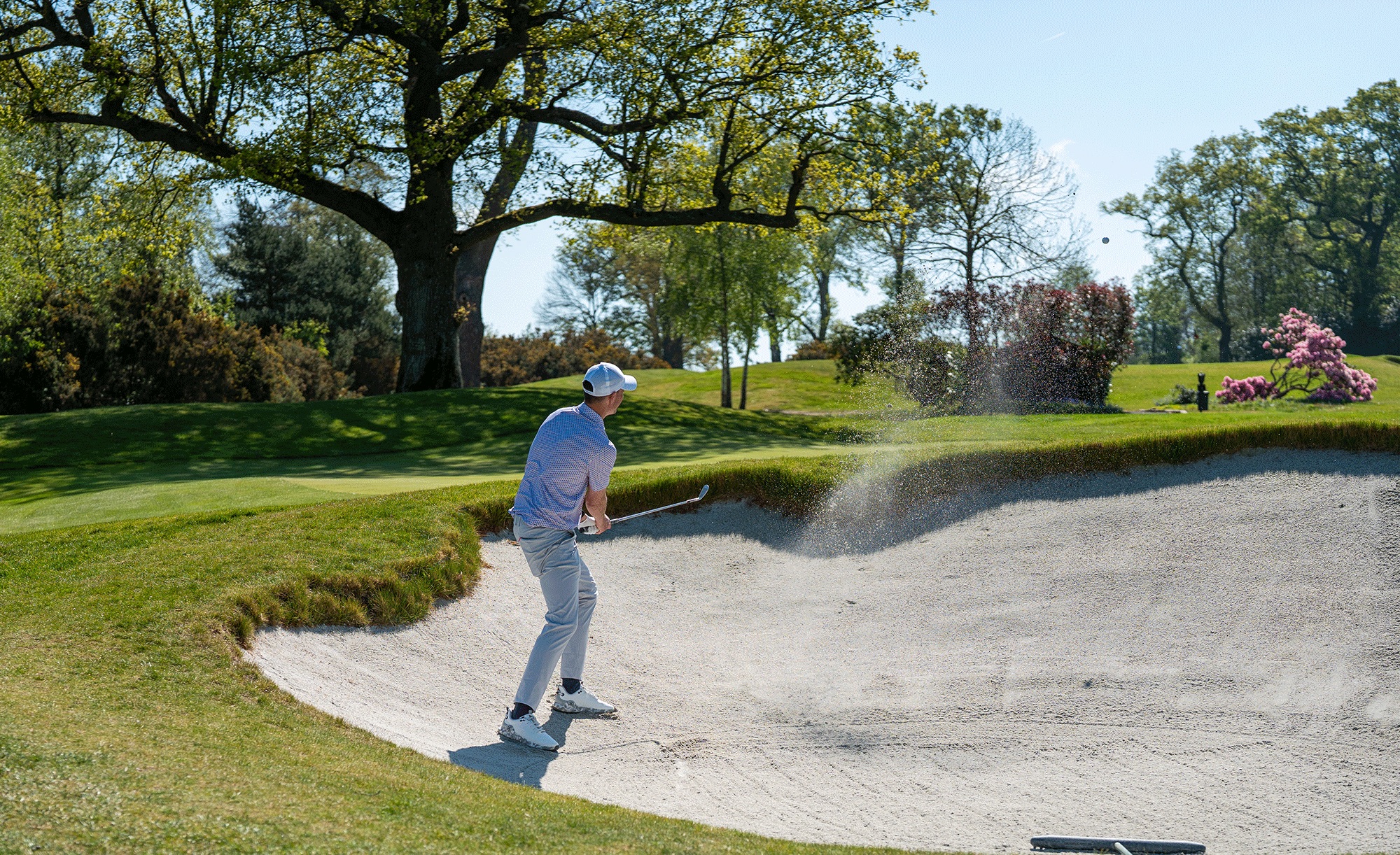 An amateur golfer hitting a bunker shot near the green
