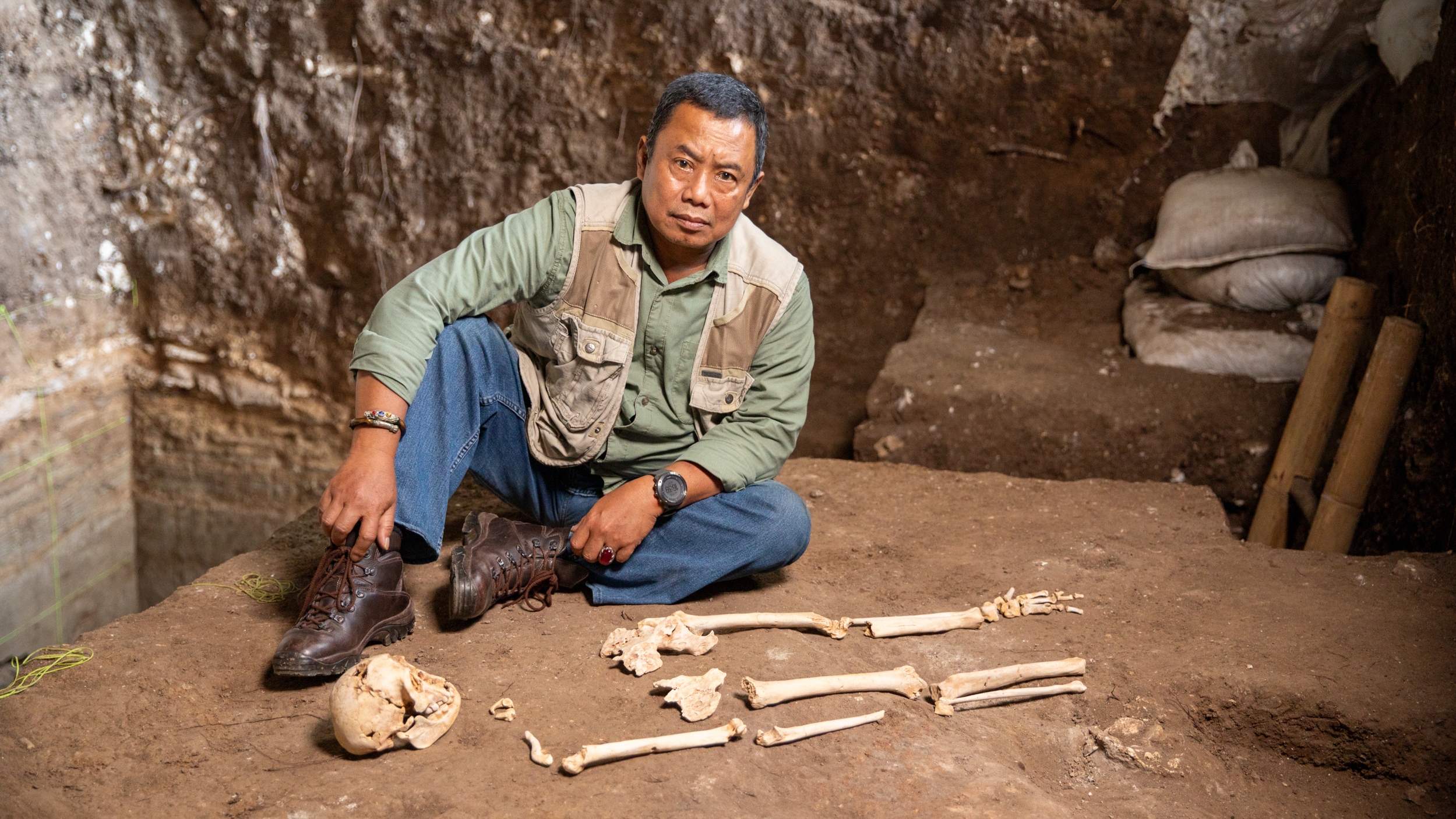 Dr Thomas Sutikna sitting alongside a replica of Homo floresiensis in Liang Bua cave, Flores, Indonesia in Human