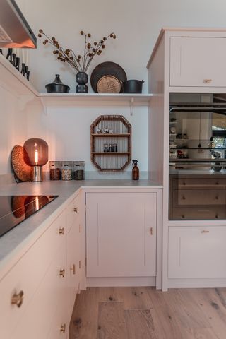 A pale pink kitchen corner with white worktops and a glass lamp