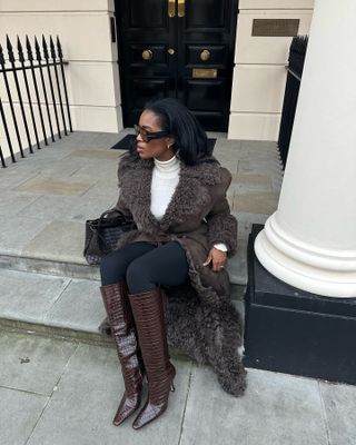 Influencer @nlmarilyn wears black leggings with brown leather knee-hgih boots and a matching brown trench coat.