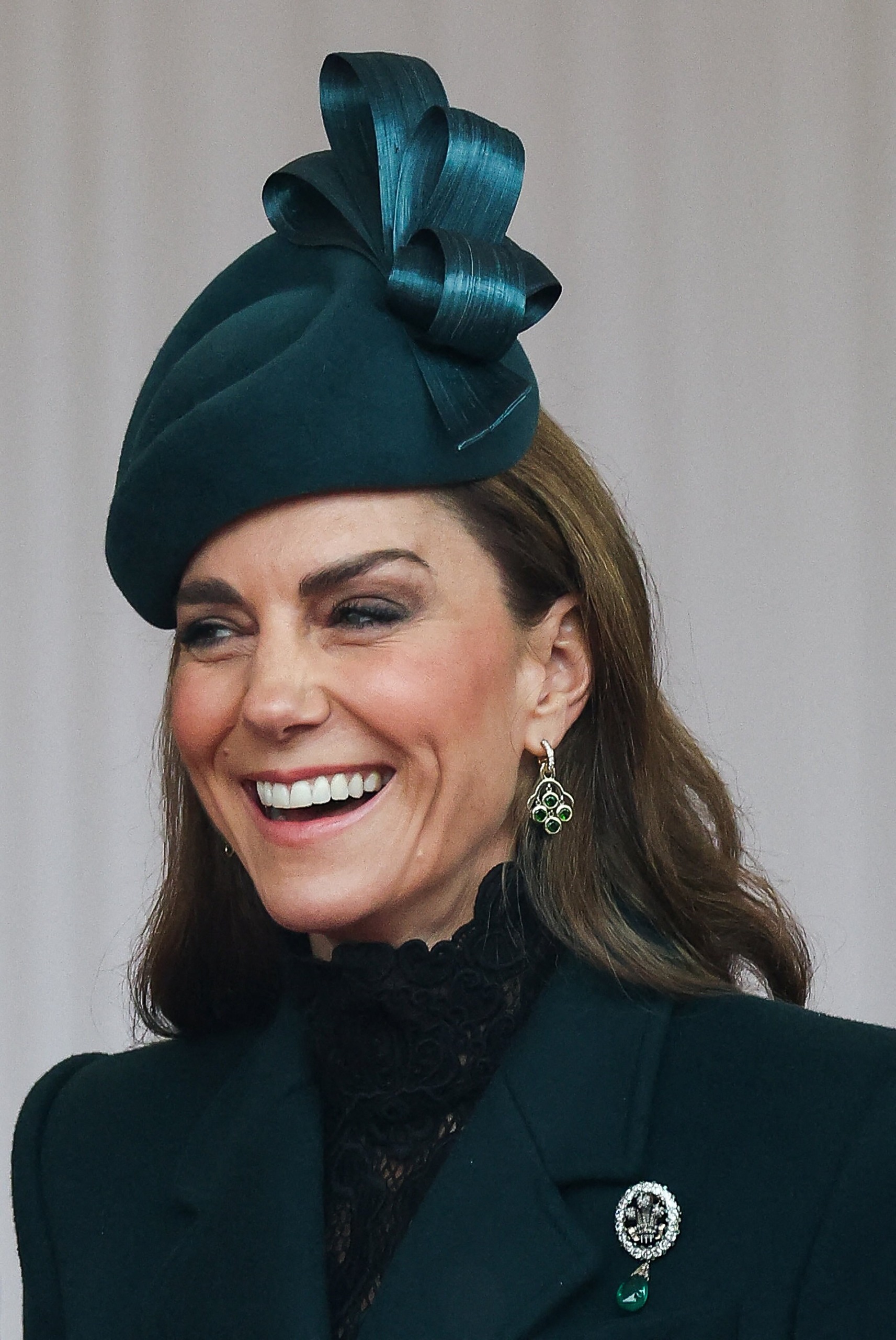 Princess Kate wearing a green coat with the Prince of Wales Feathers brooch and laughing
