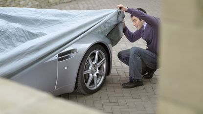 A man lifts the cover on a collectible car to look at it.