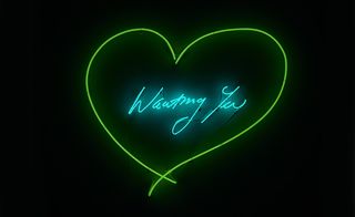 A neon sign saying 'Wanting You' in blue light, with a green heart around the writing.
