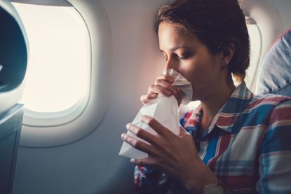 Young woman feeling bad during a flight and breathing into a bag