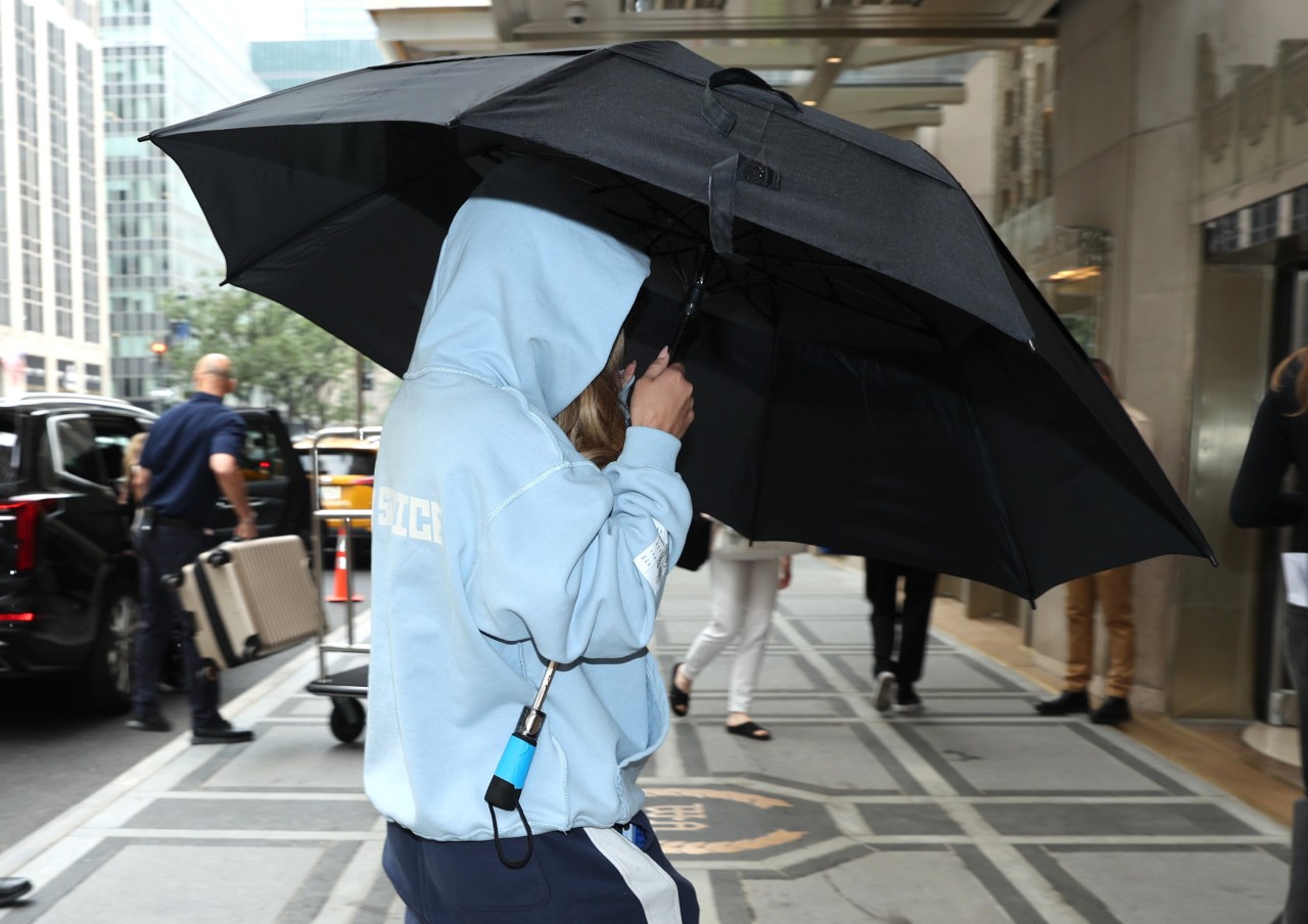 Sydney Sweeney is seen arriving on the set of "The Devil Wears Prada 2" on August 06, 2025 in New York City. She's holding a big black umbrella and her hood is up.
