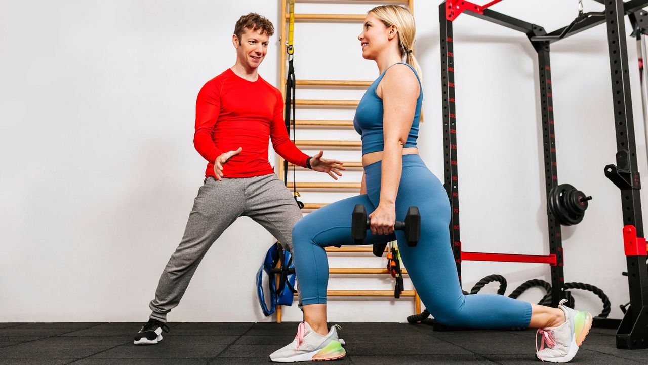 A woman performing a lunge ina gym while being watched by her coach