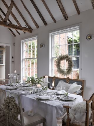 White Christmas dining room with festive settings, beaded garland, indoor wreaths, bench seating and dining chairs