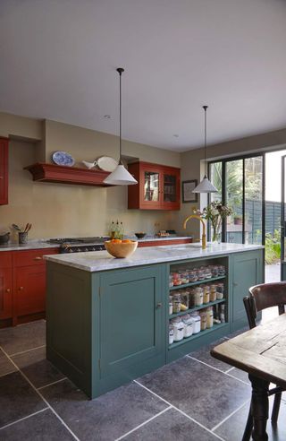 A kitchen with teal and red cabinets and natural stone flooring with white grout lines