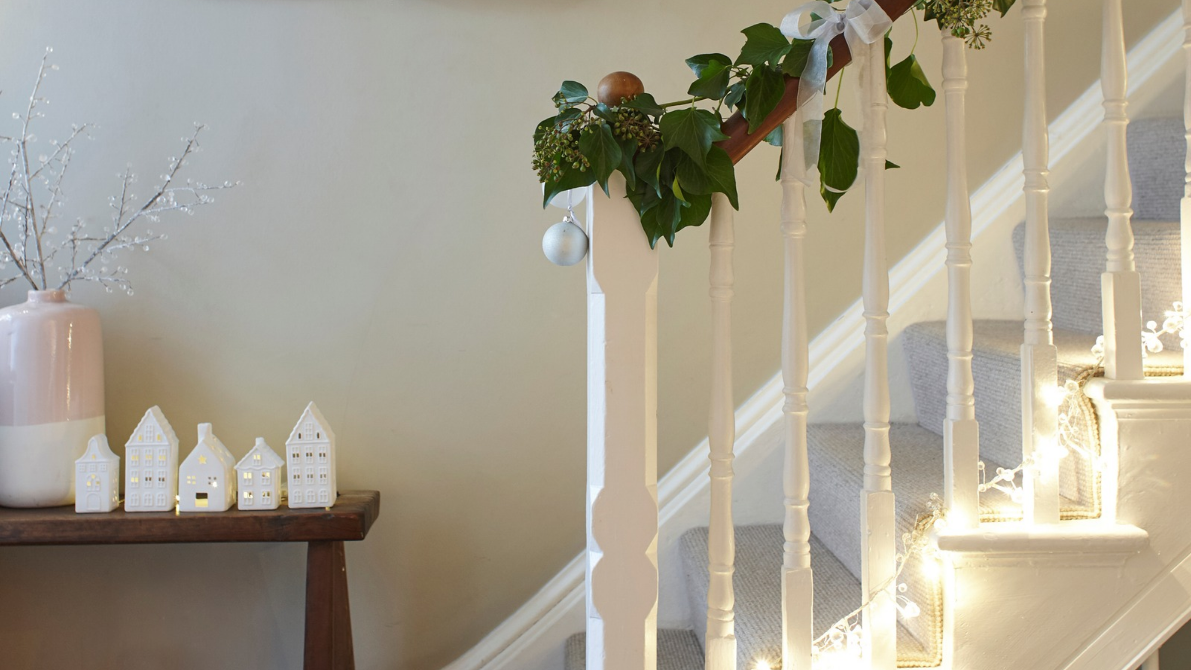 Ceramic light up houses on a side table next to a festive staircase.