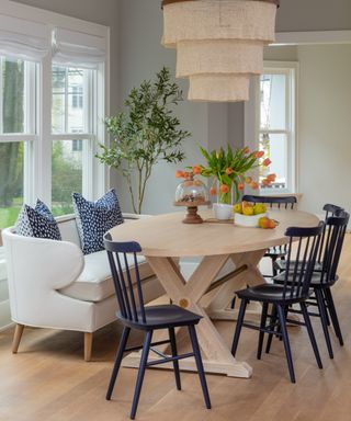 colors that go with light grey, grey dining room with blond wood oval table, navy dining chairs, couch, fruit and flowers on table, fabric and wood pendant light, navy spot couch pillows
