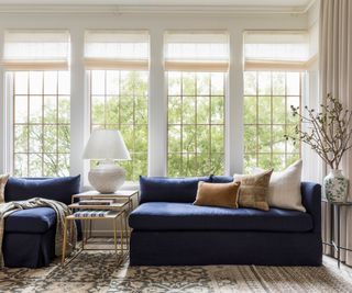 sunroom painted in neutral tones with two large navy velvet couches and vintage rug and pillows