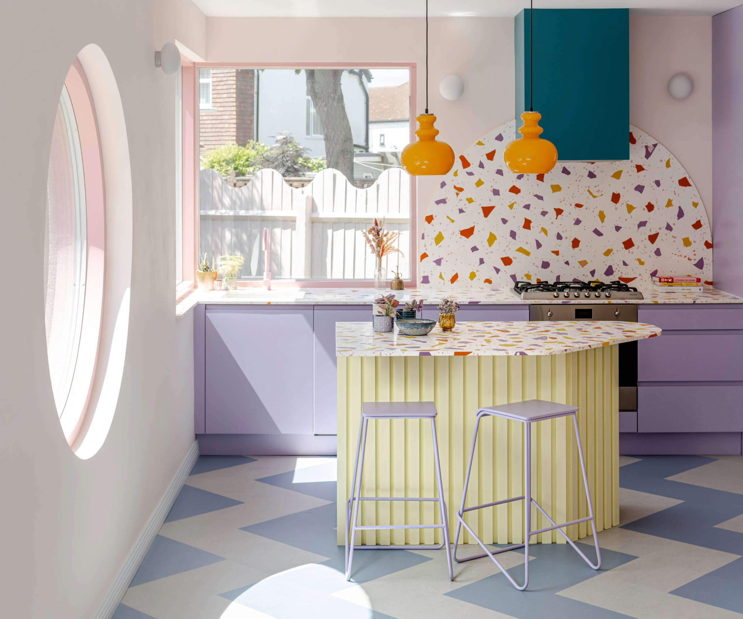 Kitchen with large circle window, blue patterned flooring, terrazzo style splashback and worktop and purple cabinets