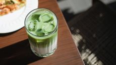 An iced matcha latte with cold foam on a wooden table, viewed from above. 