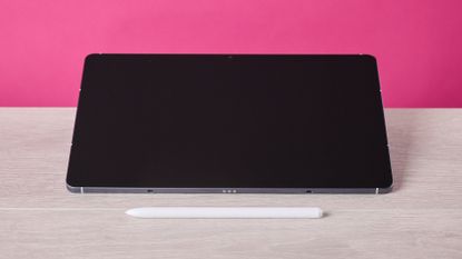 The Samsung Galaxy Tab S10 FE sat on a table behind the S Pen and in front of a pink background.