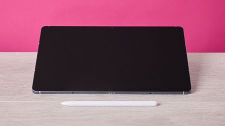 The Samsung Galaxy Tab S10 FE sat on a table behind the S Pen and in front of a pink background.