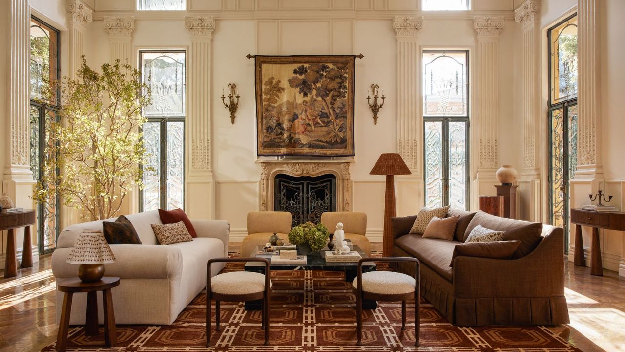 A living room with high ceilings, architectural molding, two sofas, a characterful area rug, and a mural