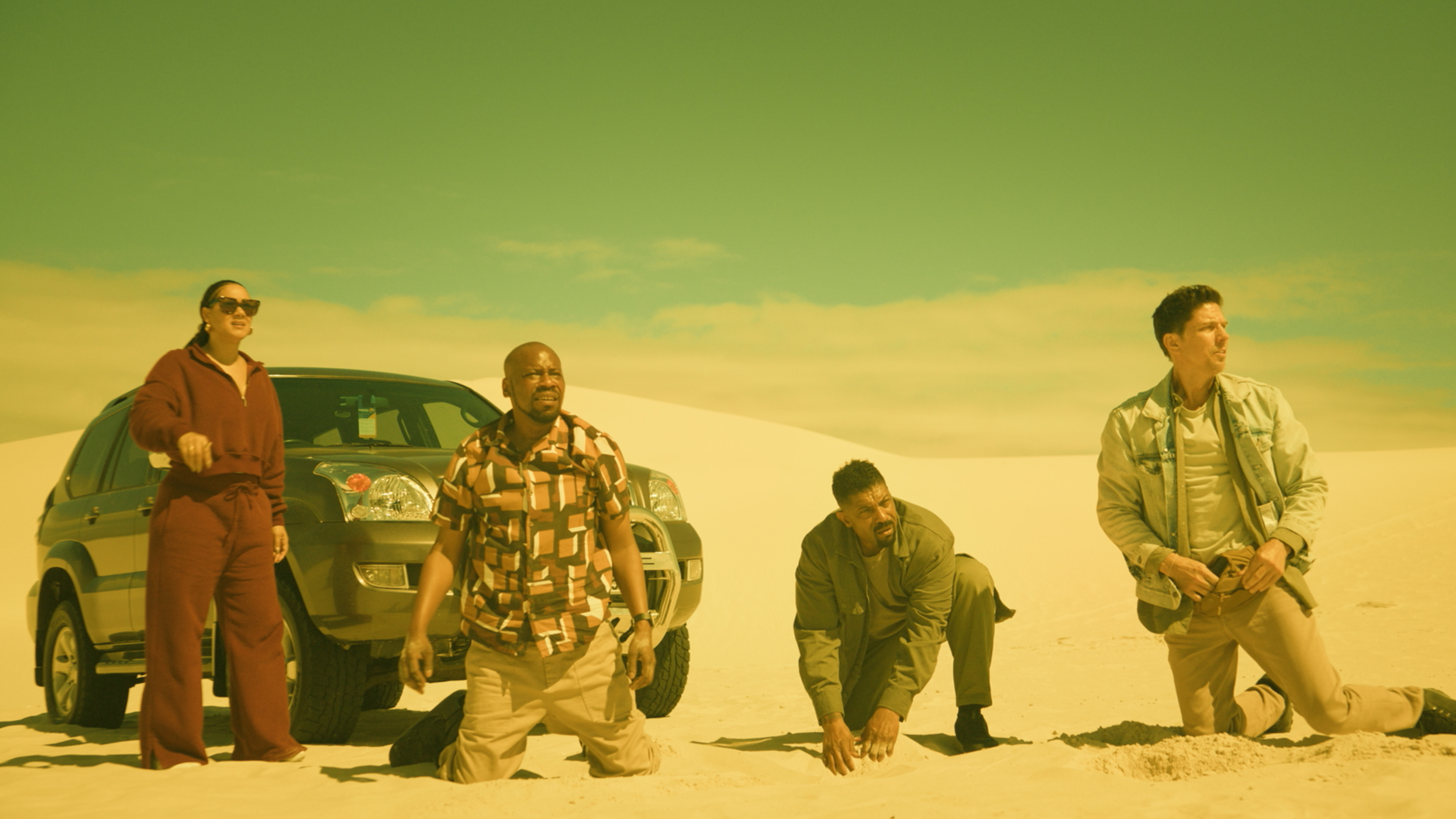 L-R: Cynthia Kaye McWilliams as Cathy Montgomery, Malcolm Barrett as Leon Montgomery, Deon Cole as Joe Washington, and Michael Trucco as Benjamin 'Touch' Tuchawuski kneeling on sand in front of a car.