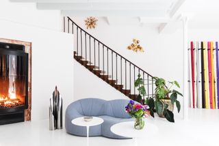 Staircase leading to open plan area with gray couch, plants, round white tables and fireplace