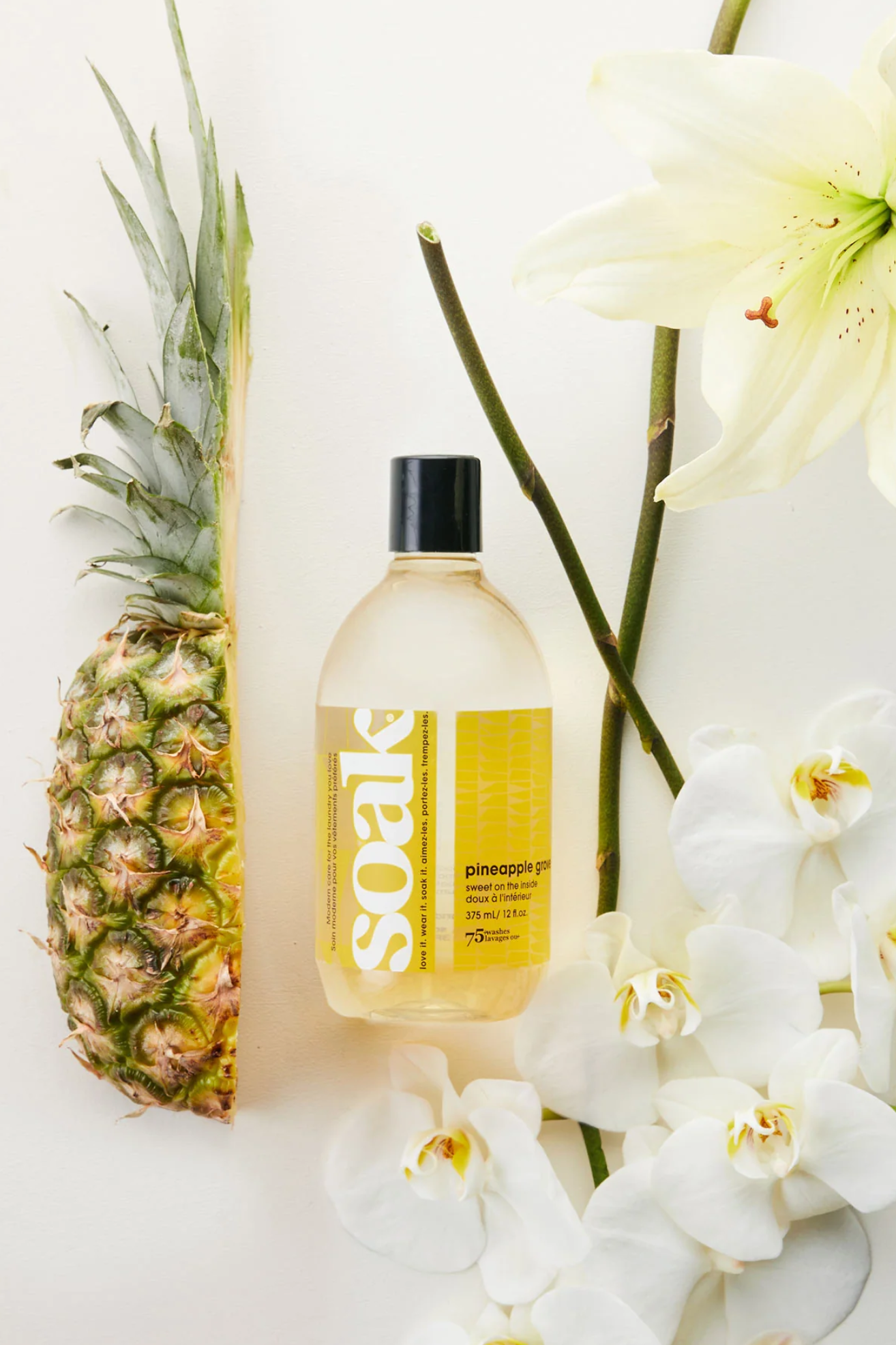 A bottle of laundry detergent near a halved pineapple and stems of orchids