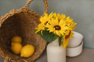 Vase with sunflowers next to ceramic bowls and a basket with fresh lemons on a table