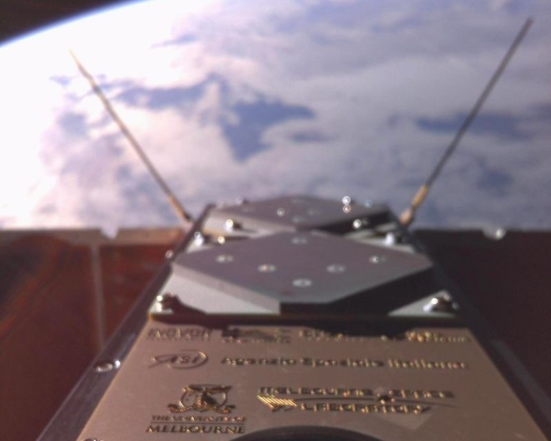 square metal surfaces and two stick-like antenna dominate the foreground of this image, with a blue-and-white earth in the background