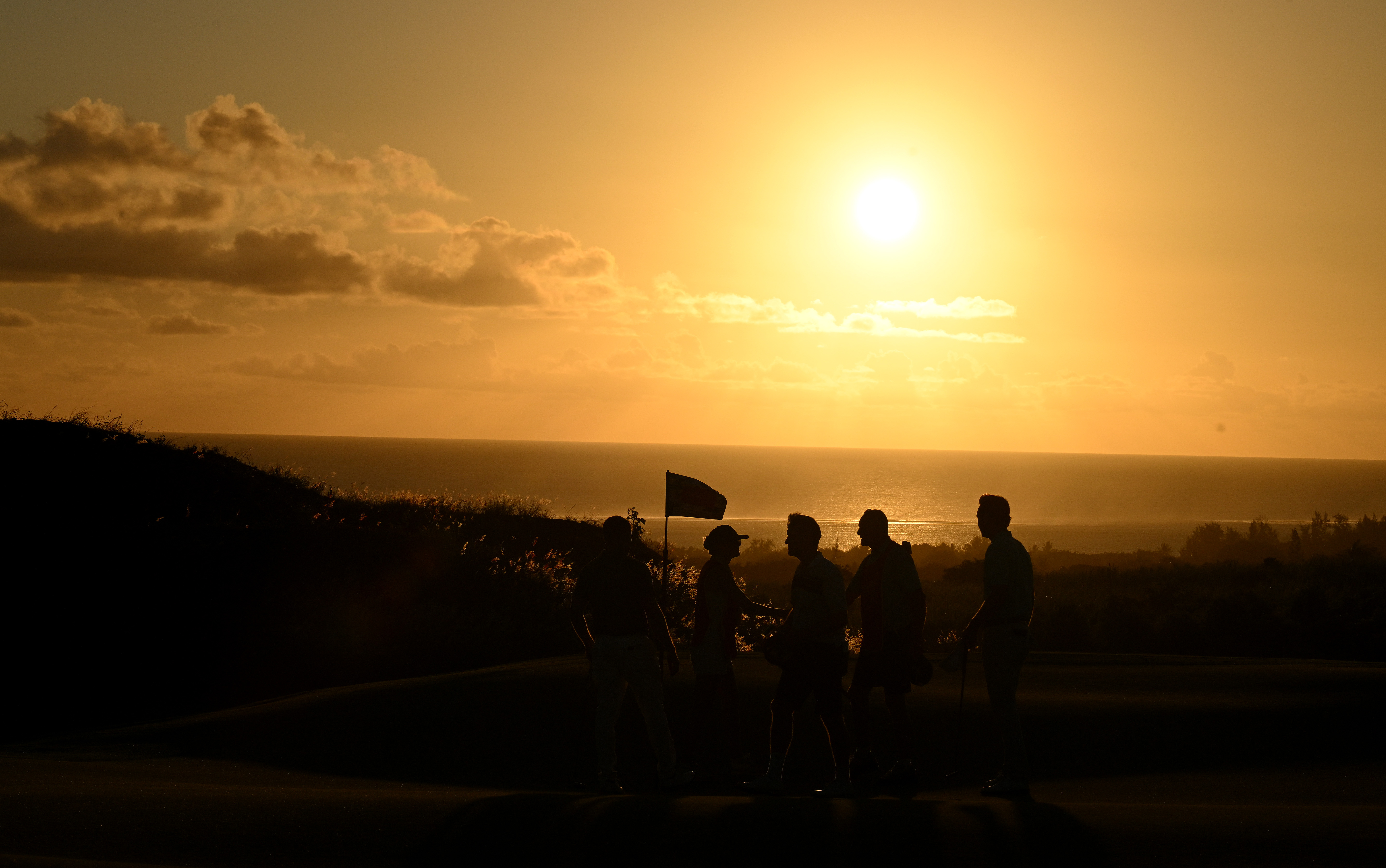 Golfers shake hands on the 18th green with a setting sun in the background